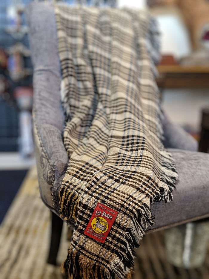 Tan, navy, and white woven cotton plaid afghan draped over a gray upholstered chair with red 5/A Baker label.