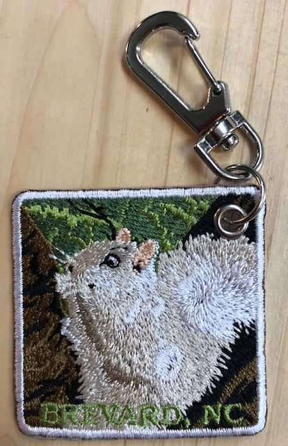 A key chain with an embroidered patch featuring a white squirrel and the text 'Brevard, NC' on one side.