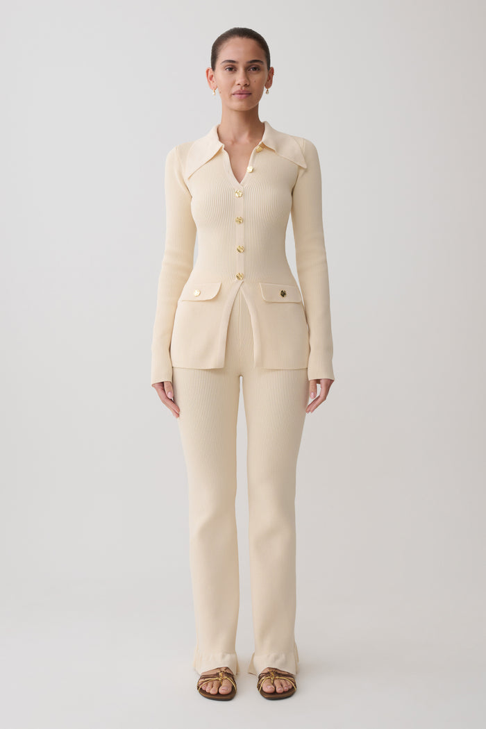 Woman wearing a white ribbed long sleeve longline top with ribbed flared pants.